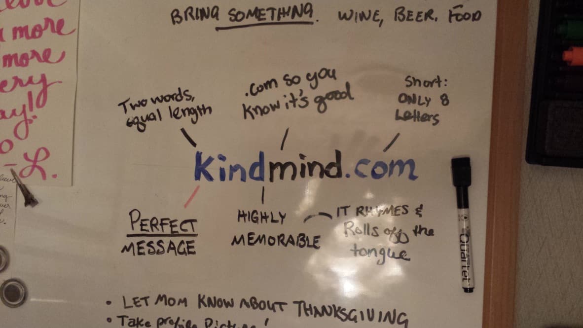 Whiteboard brainstorm about the kindmind.com domain name, annotations read: Two words equal length, .com so you know it's good, Short only 8 letters, Perfect message, Highly memorable, It rhymes and rolls off the tongue